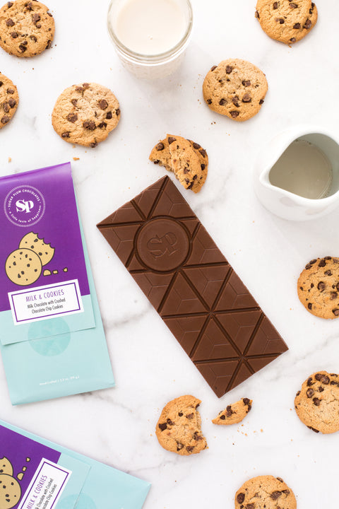 Nostalgic milk and cookies chocolate bar with cookies, glass of milk, and milk jug on marble background.