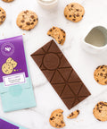 Nostalgic milk and cookies chocolate bar with cookies, glass of milk, and milk jug on marble background.