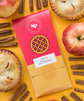 Nostalgic apple pie chocolate bar surrounded by apples, pies, and cinnamon sticks on a yellow background.