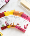 Four-pack of Butter Seasonings with flavors Lemon Garlic, Umami Butter, Sun-Dried Tomato, and Apple Cinnamon next to a stick of butter.