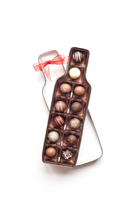 Wine bottle-shaped box with 12 handcrafted gourmet chocolate truffles, ideal gift for wine lovers, packaged with a red ribbon.