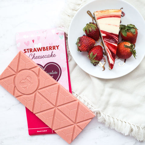 Strawberry Cheesecake White Chocolate Bar with fresh strawberries and cheesecake slice on a plate.
