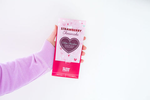 Hand holding Strawberry Cheesecake White Chocolate Bar packaging against a white background