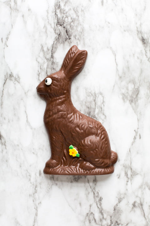 Milk Chocolate Easter Bunny with eye and spring flower decoration on marble background.