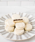 White chocolate-covered sandwich cookies arranged on a decorative plate, with one cookie showing a rich filling.