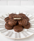 Plate of gourmet chocolate-covered sandwich cookies with a bite taken out of one, showcasing creamy filling and rich chocolate coating.