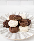 Assorted chocolate-covered sandwich cookies with milk and white chocolate drizzle, arranged on a decorative plate.