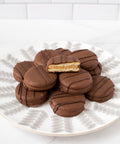 Chocolate-covered peanut butter cracker cookies on a plate, one cookie cut to show creamy milk chocolate coating and filling.