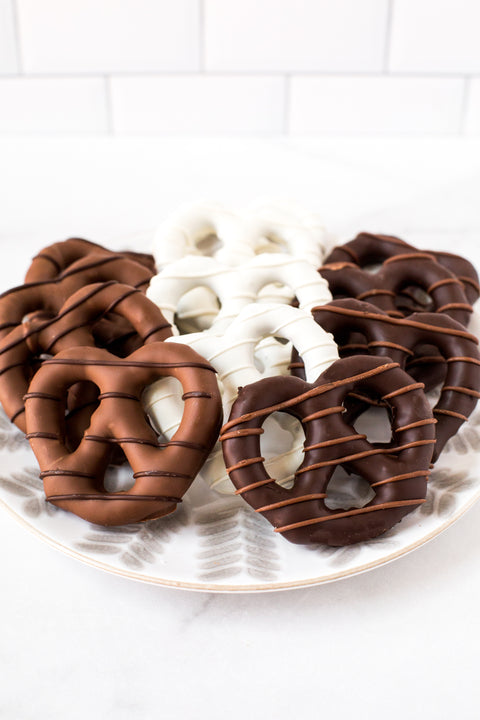 Assorted handcrafted chocolate-covered pretzels on a plate, featuring milk, dark, and white chocolate, perfect for snacking and gifting.