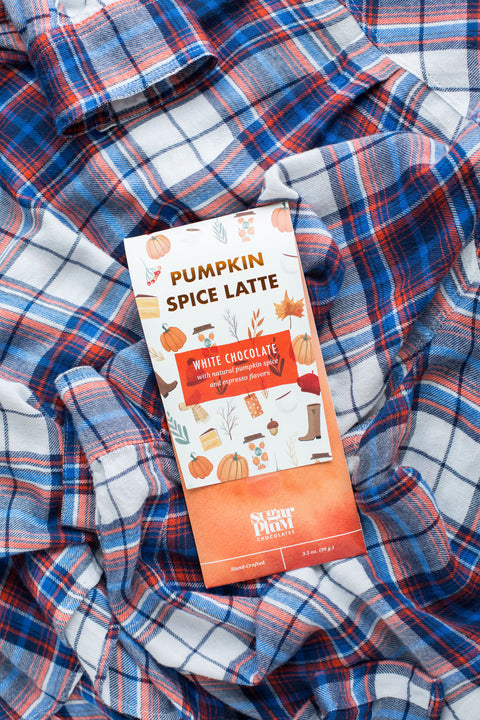 Pumpkin Spice Latte white chocolate bar on cozy plaid fabric, showcasing fall-inspired packaging with autumn-themed illustrations.