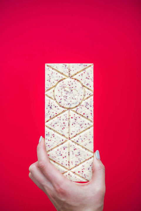 Hand holding a Candy Cane White Chocolate Bar with crushed peppermint on a vibrant red background.