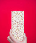 Hand holding a Candy Cane White Chocolate Bar with crushed peppermint on a vibrant red background.