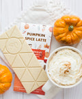 Pumpkin Spice Latte chocolate bar with white chocolate, surrounded by fall pumpkins and a whipped cream-topped latte.