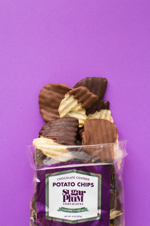 Pack of chocolate-covered potato chips against a purple background, showcasing milk and dark chocolate flavors by Sugar Plum Chocolates.
