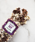 Chocolate-covered popcorn in a clear bag on a marble surface, featuring gourmet popcorn drizzled with milk and dark chocolate.