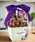 Gourmet chocolate gift basket with purple ribbon featuring cookies, popcorn, and pretzels by Sugar Plum. Ideal for special occasions.