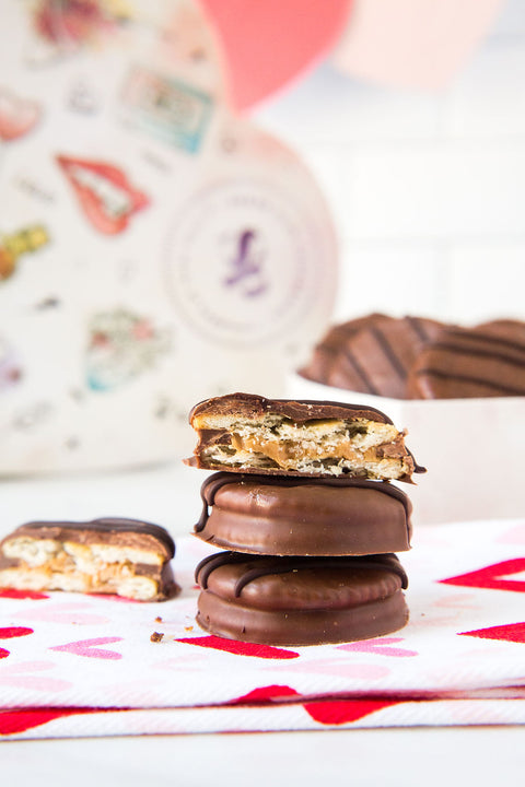 Milk chocolate-covered peanut butter cracker cookies stacked on a heart-patterned cloth with heart-shaped box in the background.