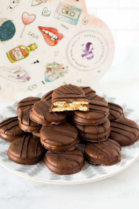Milk chocolate-covered peanut butter cracker cookies stacked on a plate in front of a decorative heart-shaped box.