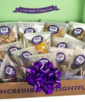 Large snack box filled with assorted treats, featuring a purple ribbon and labeled "a little taste of happiness" inside lid.