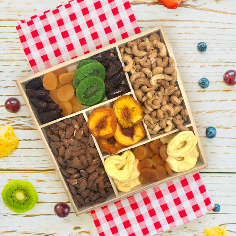 Gourmet dried fruit and nut tray on wooden platter with apricots, dates, kiwis, peaches, apples, cashews, and smoked almonds.