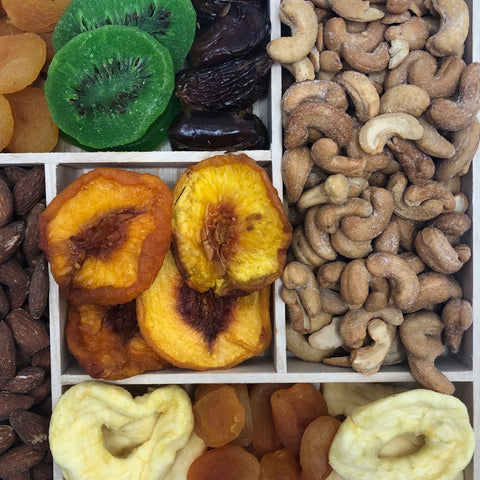 Gourmet dried fruit and nut tray with apricots, kiwis, dates, peaches, apples, cashews, and almonds on a wooden platter.