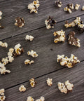 Gourmet chocolate-covered popcorn scattered on a wooden surface, showcasing a sweet and salty snack blend of milk and dark chocolate.