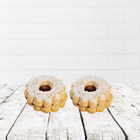 Two powdered sugar cookies on a rustic wooden table in front of a white tile background.