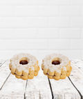 Two powdered sugar cookies on a rustic wooden table in front of a white tile background.