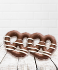 Milk chocolate covered pretzels drizzled with white chocolate on a wooden surface.