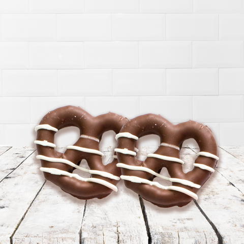 Milk chocolate covered pretzels drizzled with white chocolate on a wooden surface.