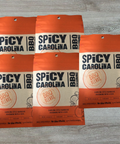 Five packs of Spicy Carolina BBQ Seasoning with vinegar and pepper blend on a wooden table.