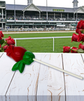Red rose lollipop on a table with a Kentucky Derby racetrack in the background.