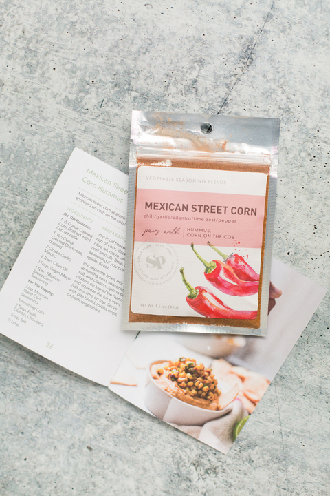 Mexican Street Corn seasoning packet with recipe cards on a gray surface, showcasing handcrafted spice blend for corn and hummus.