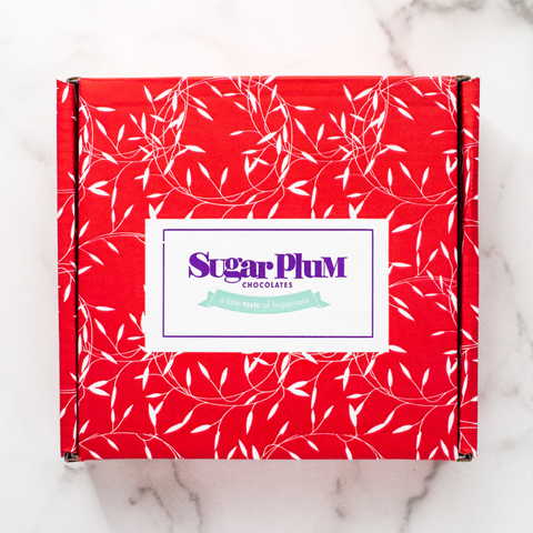 Red gift box adorned with white leaf patterns, featuring the Sugar Plum Chocolates logo on the front.