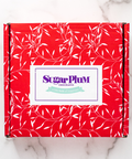 Red gift box adorned with white leaf patterns, featuring the Sugar Plum Chocolates logo on the front.