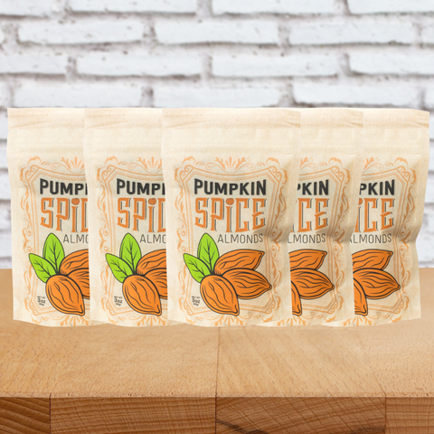 Five bags of kettle-cooked pumpkin spice almonds on a wooden table with a brick wall background.